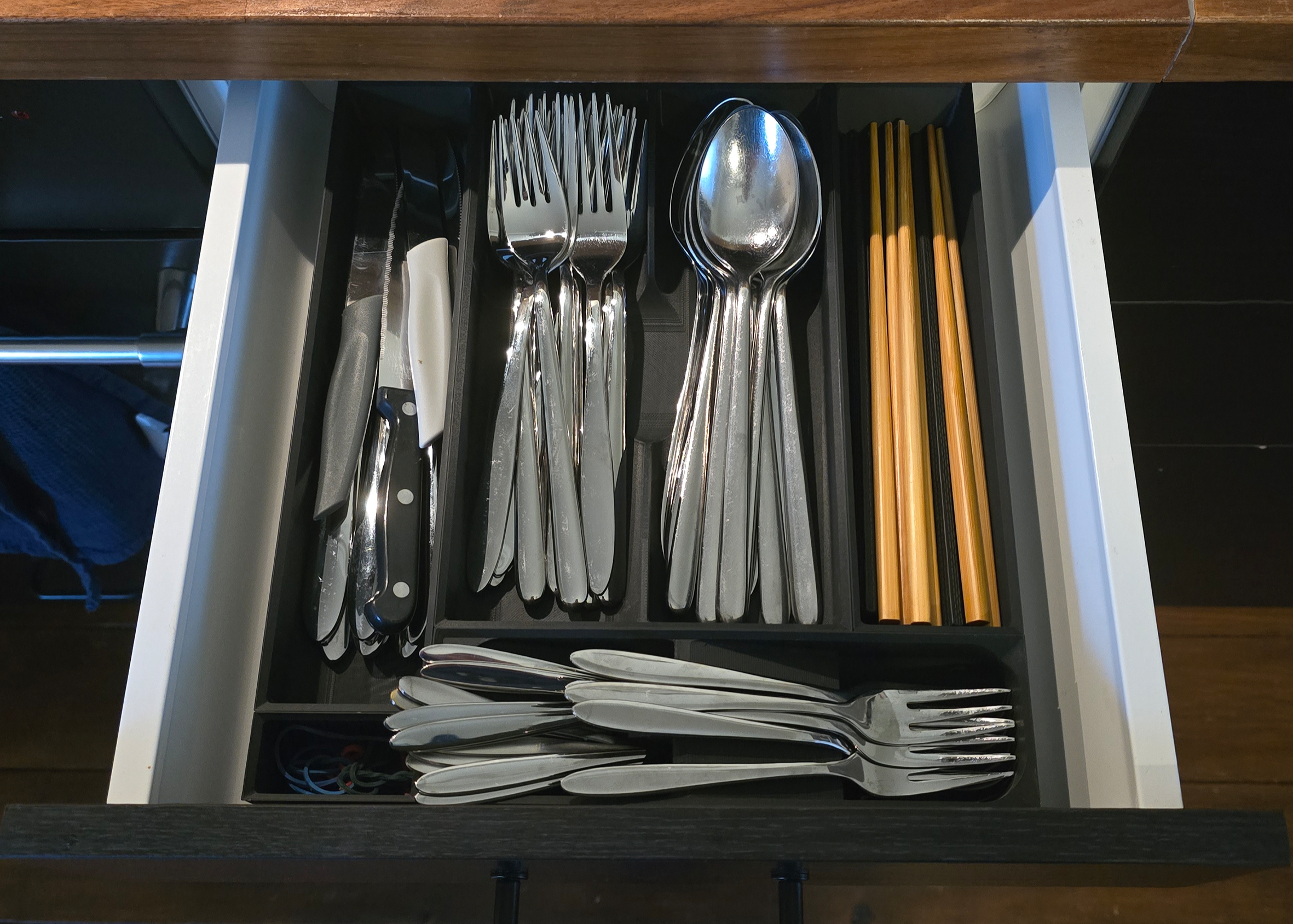 Organized kitchen drawer with neatly arranged cutlery, including knives, forks, spoons, and chopsticks in modular storage compartments